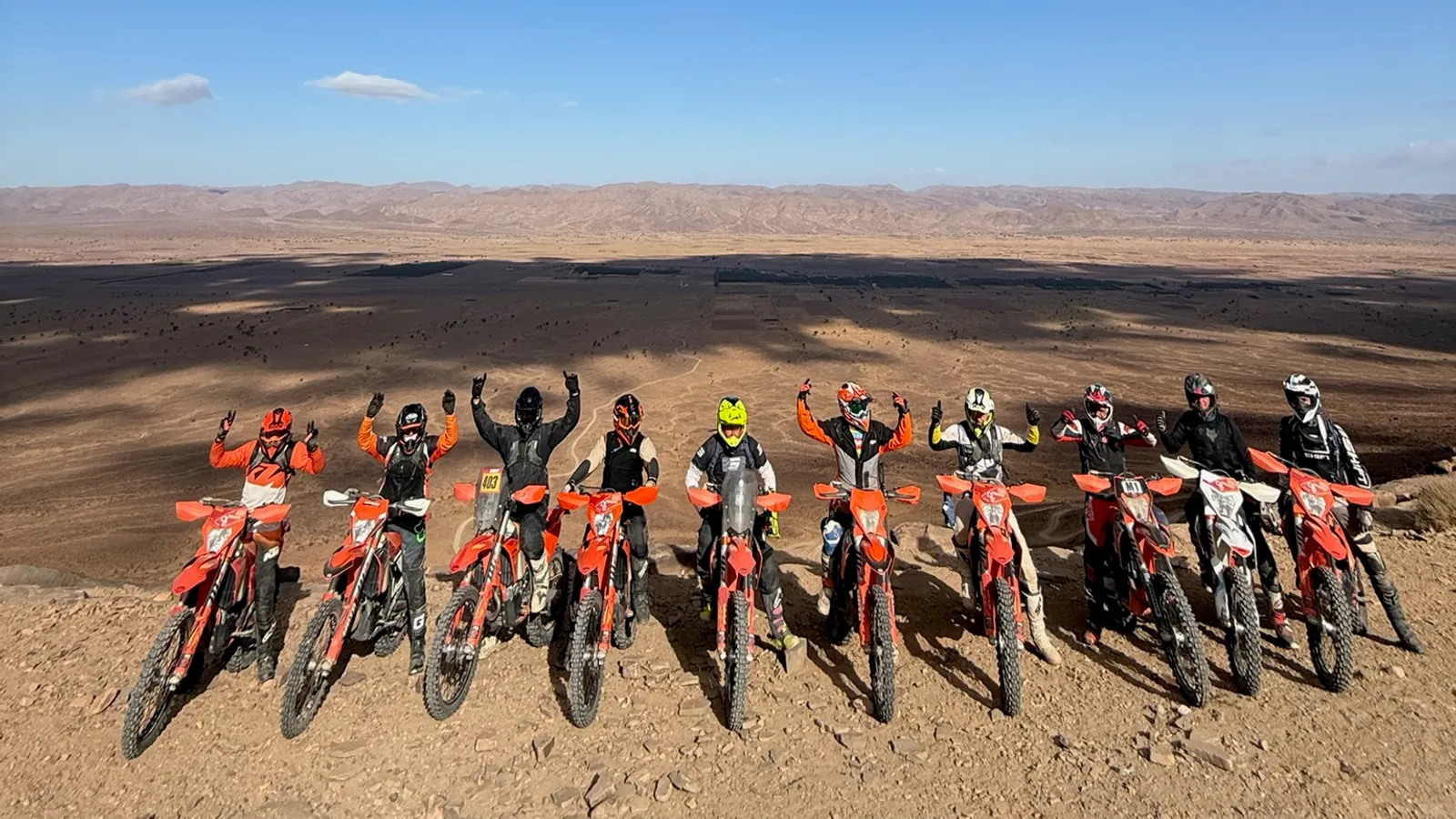 Groupe de pilotes enduro aligné sur une crête, désert marocain en toile de fond