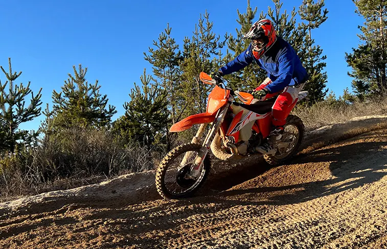 Pilote qui carve un virage sablonneux, forêt de pins et ciel bleu