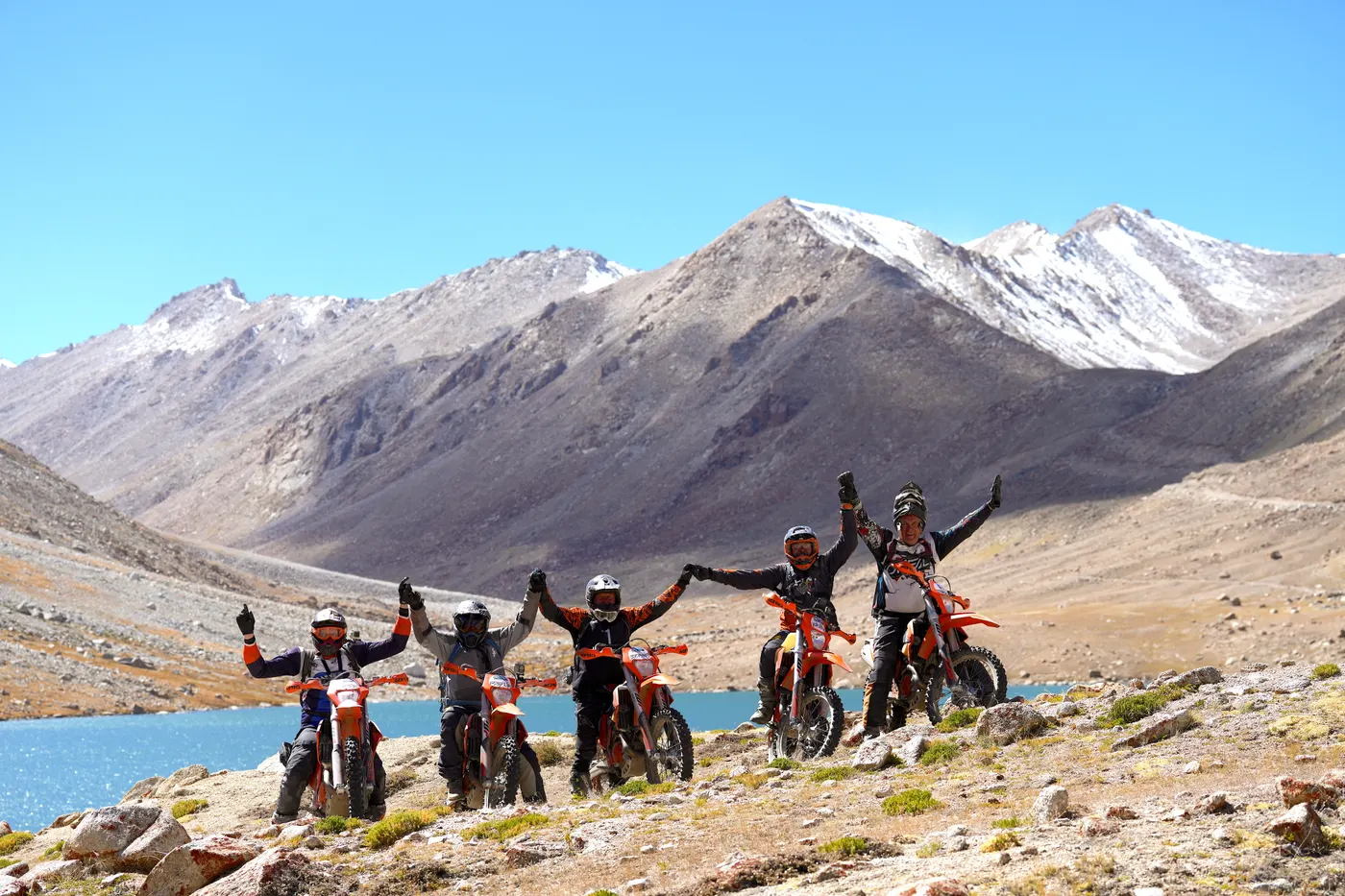 Groupe de pilotes face à un lac turquoise et des sommets enneigés